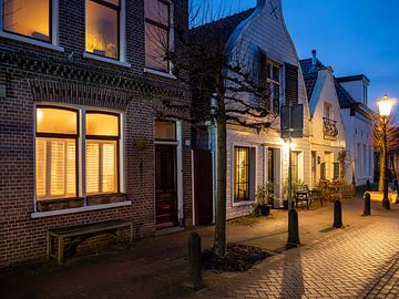 Rue du village hollandaise en soirée avec des fenêtres illuminées, des lampadaires et un ciel bleu. sur Jan Willem de Groot Photography