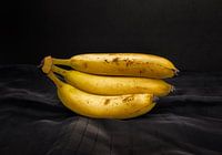 Een tros van drie bananen op een mooi belichte donkere ondergrond.