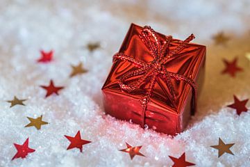 Small Christmas present box with star shape ornaments over snow by Alex Winter