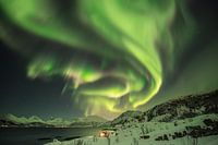 Maison dans un fjord en Norvège, sous une aurore.