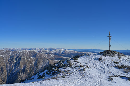 Une croix de sommet sur un sommet enneigé, sous un ciel d'un bleu éclatant