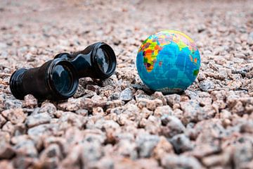 Binoculars with a small earth on pebbles in summer by Denny Gruner