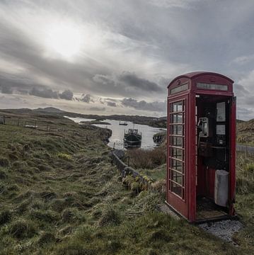 Ouderwetse telefooncel in leeg landschap met boot op achtergrond