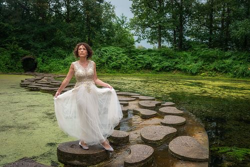 Mooie vrouw in prinsessenjurk op stapstenen van Gé Klein Wolterink