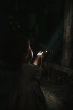 Magie maken. Klein meisje speelt met stof en een straal zonlicht van Ayla Maagdenberg