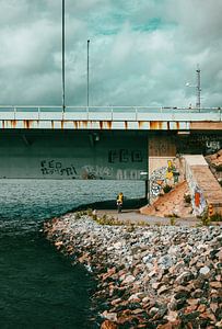 Radfahrer unter der Brücke – Türkiser Himmel & raue Uferlinie