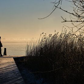 Eenzaam wandelende  fotograaf langs het bevroren meer bij zonsopkomst in koude winter van BJ Fleers