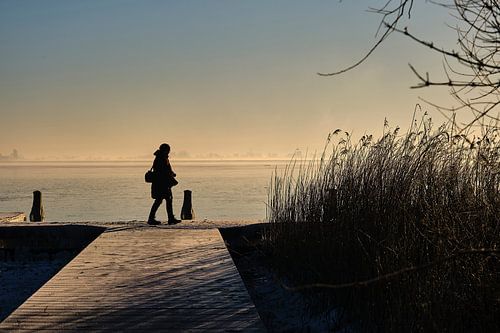 Lonely walking photographer along the frozen lake at sunrise in cold winter