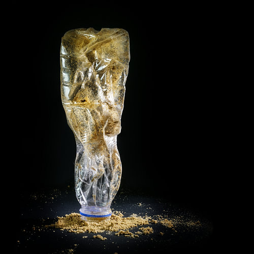 Weggeworfene Plastikflasche mit Sand vom Strand, dargestellt wie eine Kunstskulptur vor schwarzem Hi
