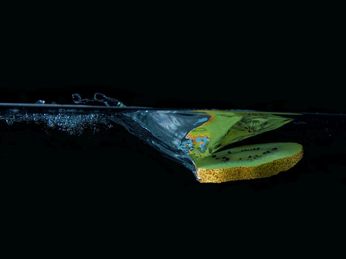 Kiwi in het water – fruitige plons tegen een zwarte achtergrond