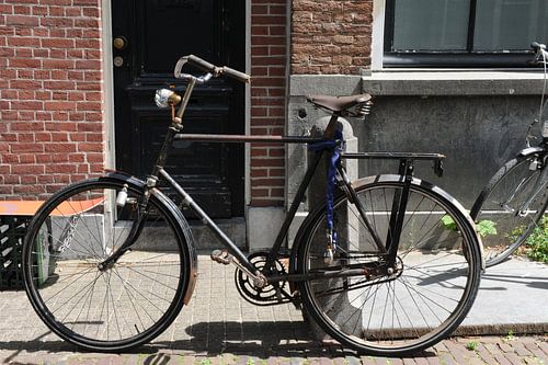 Herenfiets tegen paal aan gracht in Delft