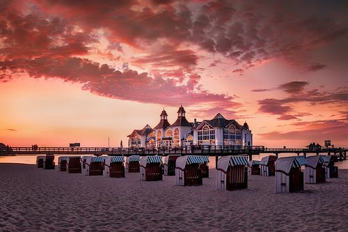 Strand met strandstoelen en pier op Rügen bij zonsondergang