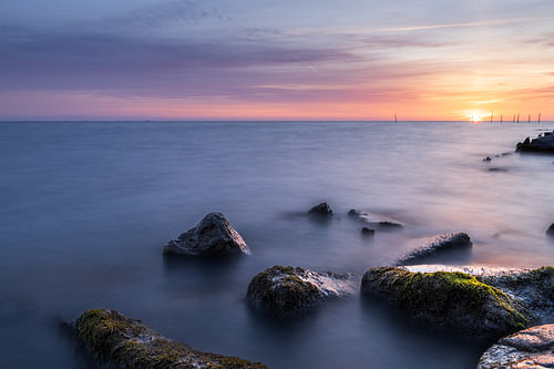 Dromerig kustlandschap met kleurrijke wolkenlucht en stenen aan de oever van het Markermeer bij Edam in Noord-Holland