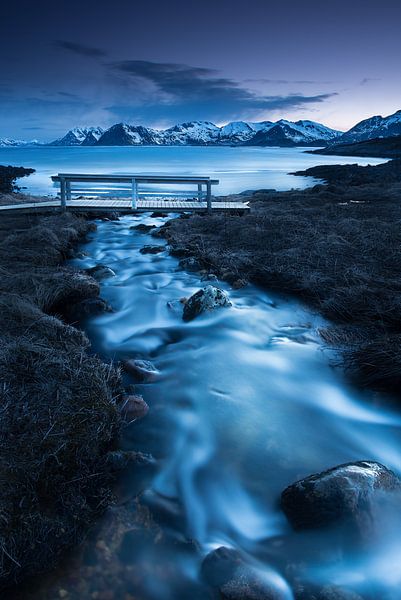 Stream with small wooden bridge in front of sea and mountains in Norway. by Voss Fine Art Fotografie