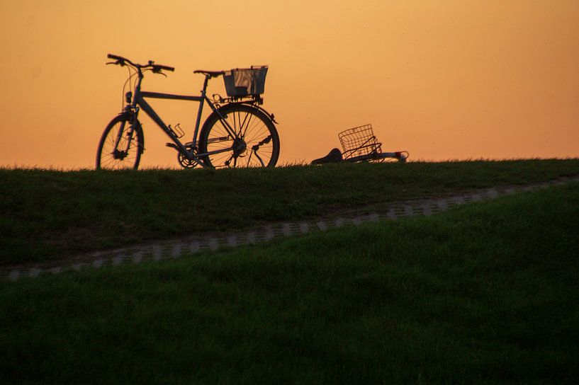 Bicycle on dike against setting sun by wil spijker