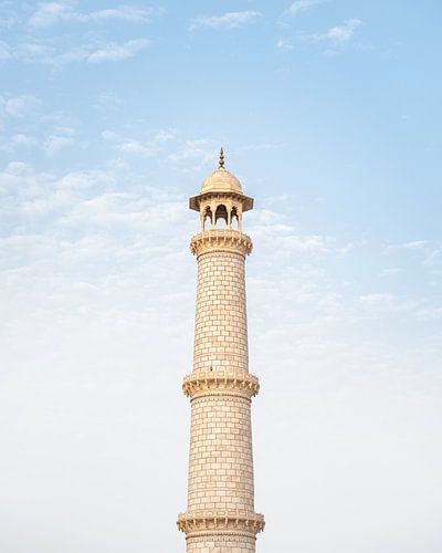 White marble tower of the Taj Mahal against the bright blue sky.