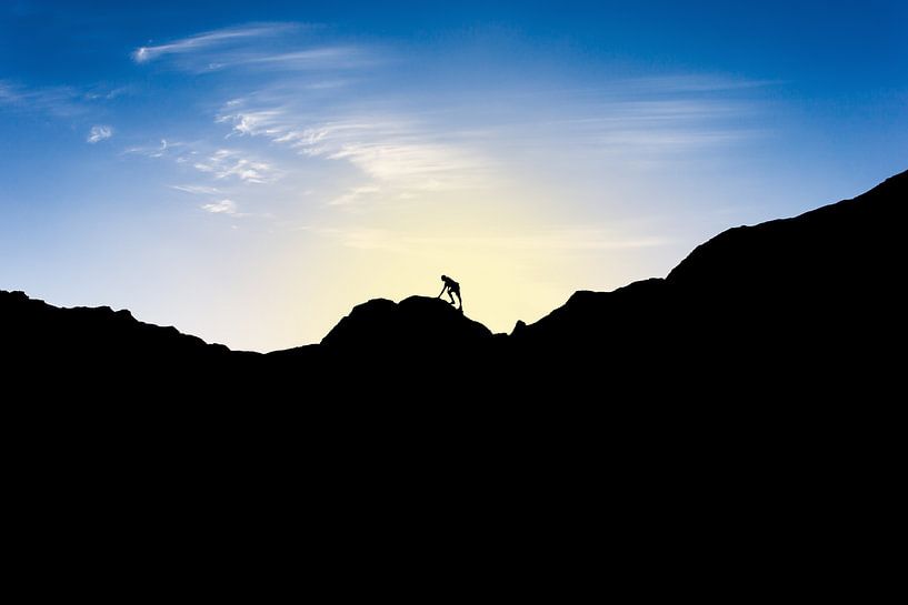 Silhouette van man die berg beklimt bij ondergaande zon. Wout Kok One2expose van Wout Kok