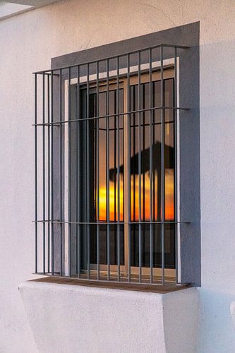 Zonsondergang weerspiegeld in een raam van een witte gevel. Rota, Costa de la Lutz, Cádiz, Andalusië, Spanje