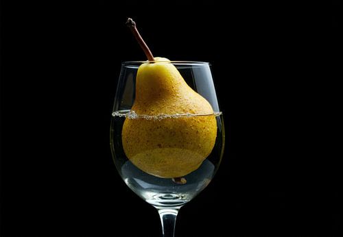Gele peer ondergedompeld in met water gevuld wijnglas