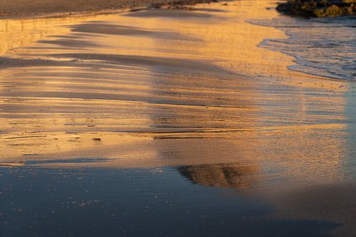 Reflectie van het avondlicht in het natte zand