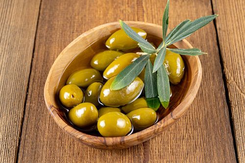 Groene olijven met twijgje in een houten schaaltje