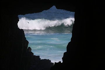 Breaking wave and flying bird, seen through a cave by Lau de Winter