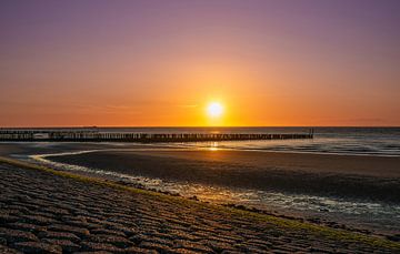 Sfeervolle warme zonsondergang aan de kust in Zeeland met paaltjes in de zee. van Wildlife Designs