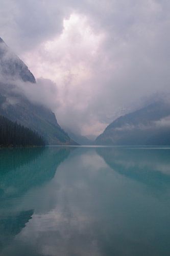 Gelassener dunkler See mit Spiegelung der majestätischen Berge in einer nebligen Umgebung