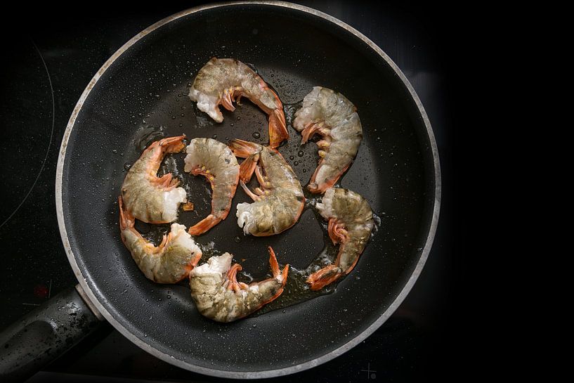 juicy fresh black tiger prawn shrimps are roasted in a black pan on the stove, cooking a tasty meal  by Maren Winter