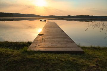 A wooden jetty on the lake in the morning mist, flooded with sunlight and a calm reflection. by Martin Köbsch