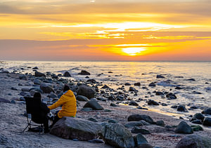 Junges Paar in gelben Regenjacken an einem Kiesstrand mit Felsen bei Sonnenuntergang auf der Ostseeinsel Rügen
