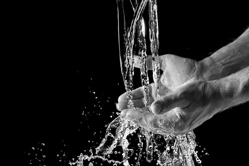 Wasser spritzt in menschliche Hände vor einem schwarzen Hintergrund mit Kopierraum, ausgewählter Fok