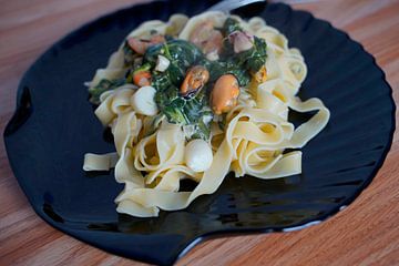 Fettuccini mit Spinat-Käse-Sahnesauce und Meeresfrüchten auf einem Teller angerichtet