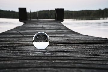 Glazen bol op een loopbrug die in een meer reikt van Martin Köbsch