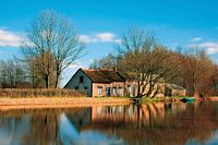 Oud huisje gespiegeld in het water van de boezem