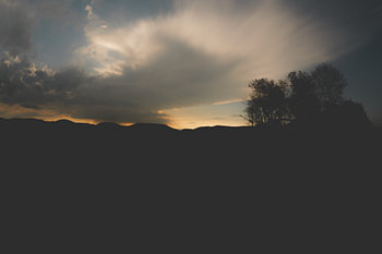 A dramatic sunset over a dark, undulating landscape