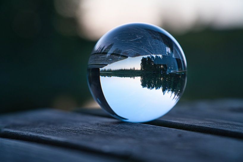 Glass ball on a footbridge reaching into a lake by Martin Köbsch