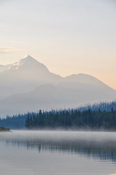 A serene lake in Canada, surrounded by majestic mountains and lush green trees, under a blue sky during sunrise, with dew on the surface of the water. The calm water reflects the landscape, creating a sense of symmetry and balance. The landscape exudes peace and serenity. This is a photo of Maligne lake in Canada. The sunrise gives it beautiful saturated hues. by UMA Digital NL