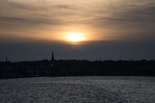 Zonsondergang boven de zee met bootspoor en silhouet aan de horizon