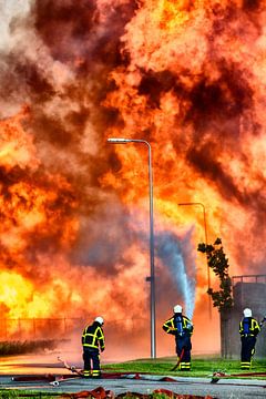 Fire fighters in front of a fire in an industrial area