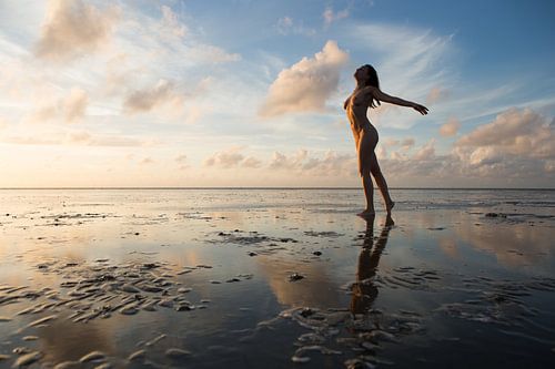Artistiek naakt op het wad met mooie luchten die spiegelen in het wad