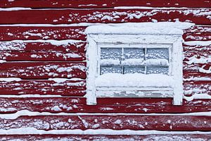 Verschneites Fenster in einem roten Holzhaus