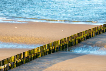 Ein menschenleerer Strand bei Zoutelande mit einer Reihe von Wellenbrechern