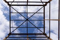Urbex symmetrie- verroeste metalen constructie tegen een blauwe lucht met wolken