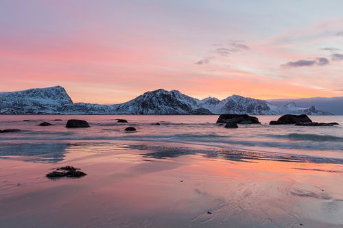 Der Sonnenuntergang hüllt das Meer und einen Strand mit Felsen in einen orangefarbenen Schein.
