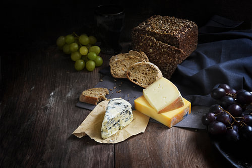 rustikales Essen mit verschiedenen Käsesorten, Vollkornbrot und Trauben auf einem dunklen Holztisch,