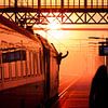 Silhouette van trein machinist die vertreksein geeft tijdens zonsondergang van Rob Kints