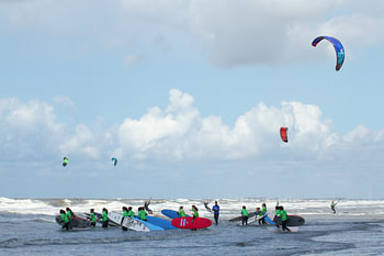 Kleurige surfplanken, kitesurfers en surfkleding bij les in de branding bij Zandvoort aan Zee