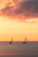 Segelboote vor einem orangefarbenen, bewölkten Himmel