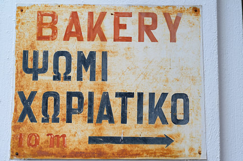 An old, rusty metal sign indicating a Greek bakery